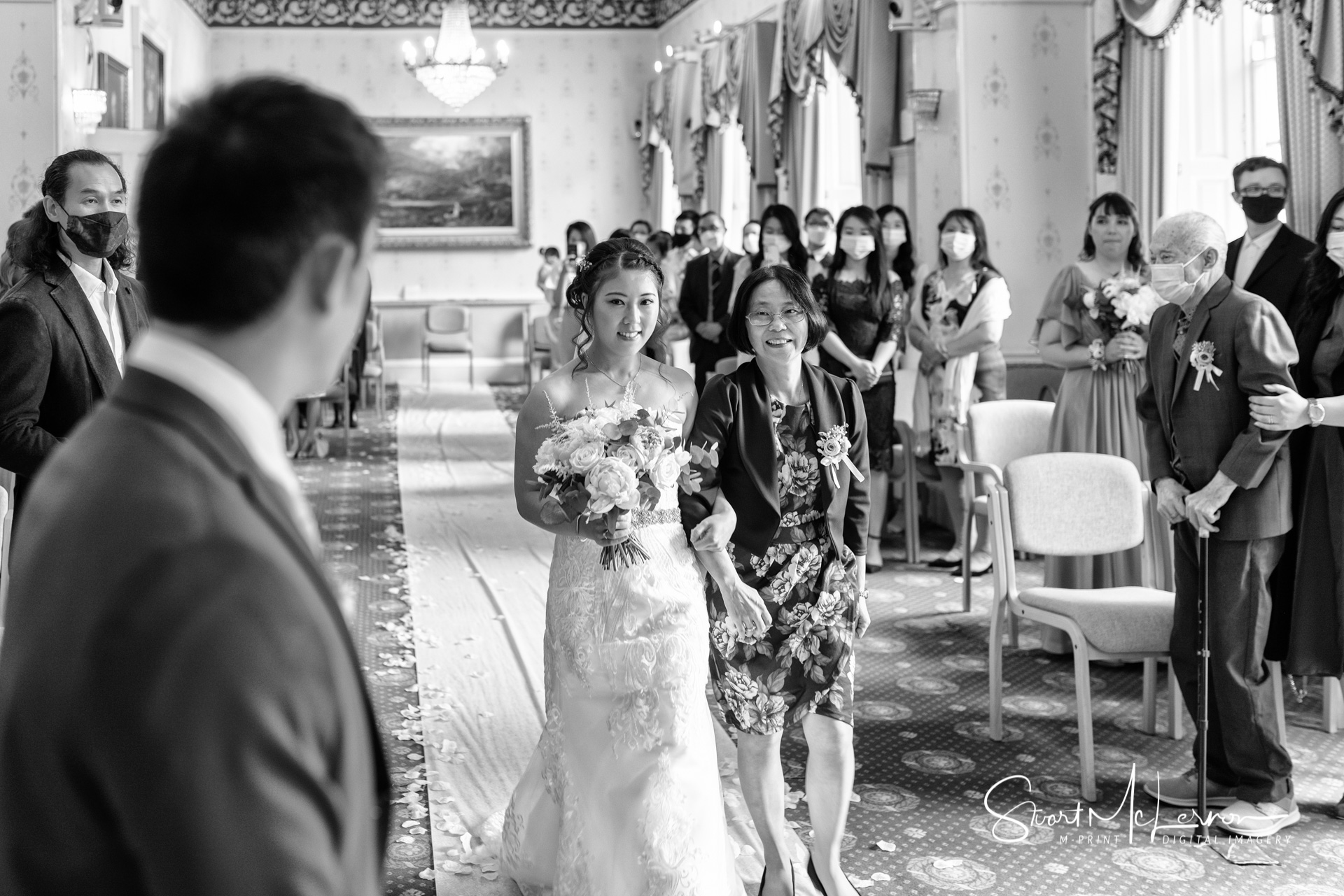 The groom watches his bride being led up the aisle by her mother at Warrington Town Hall