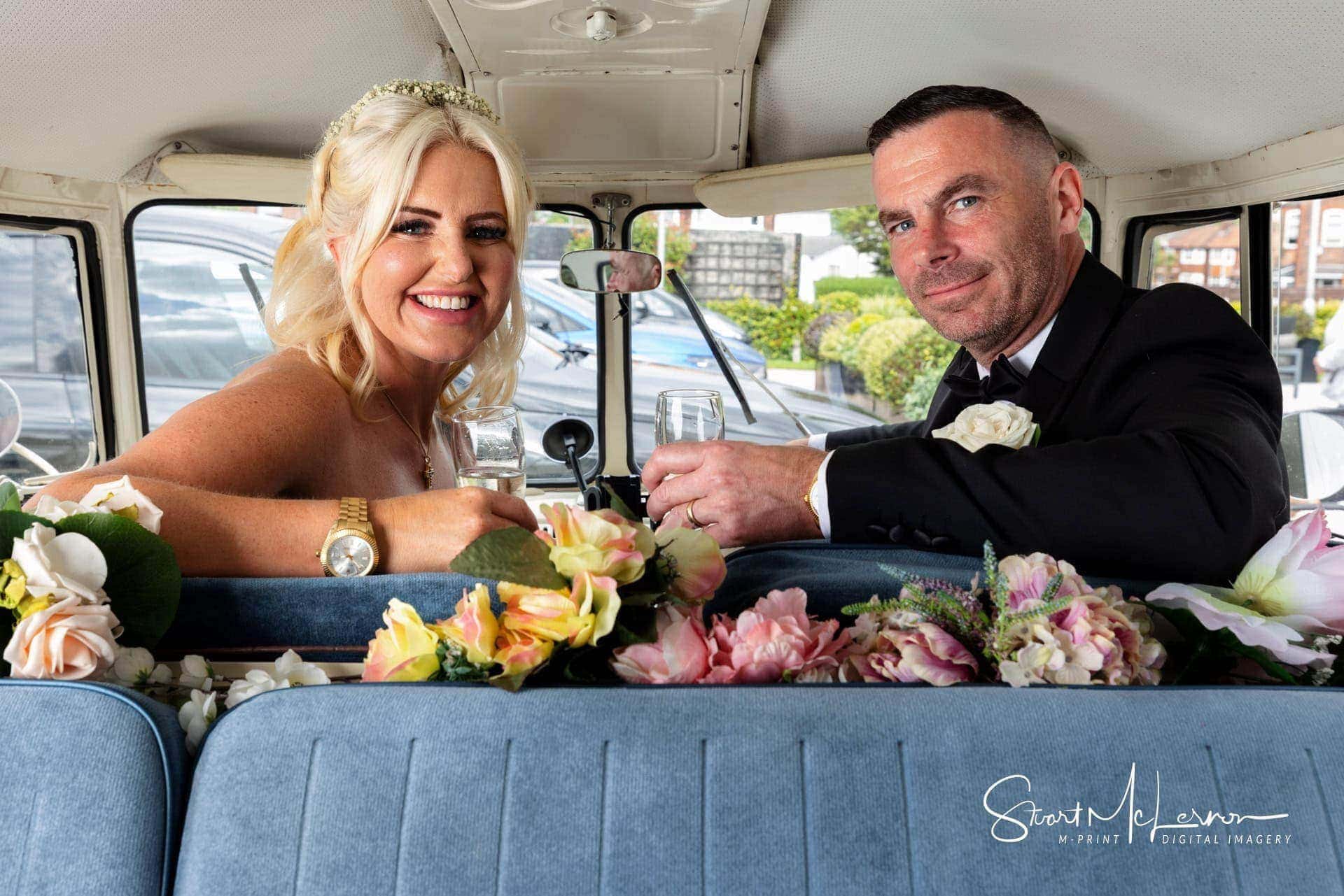 The happy couple make a toast together in the front seat of a camper van