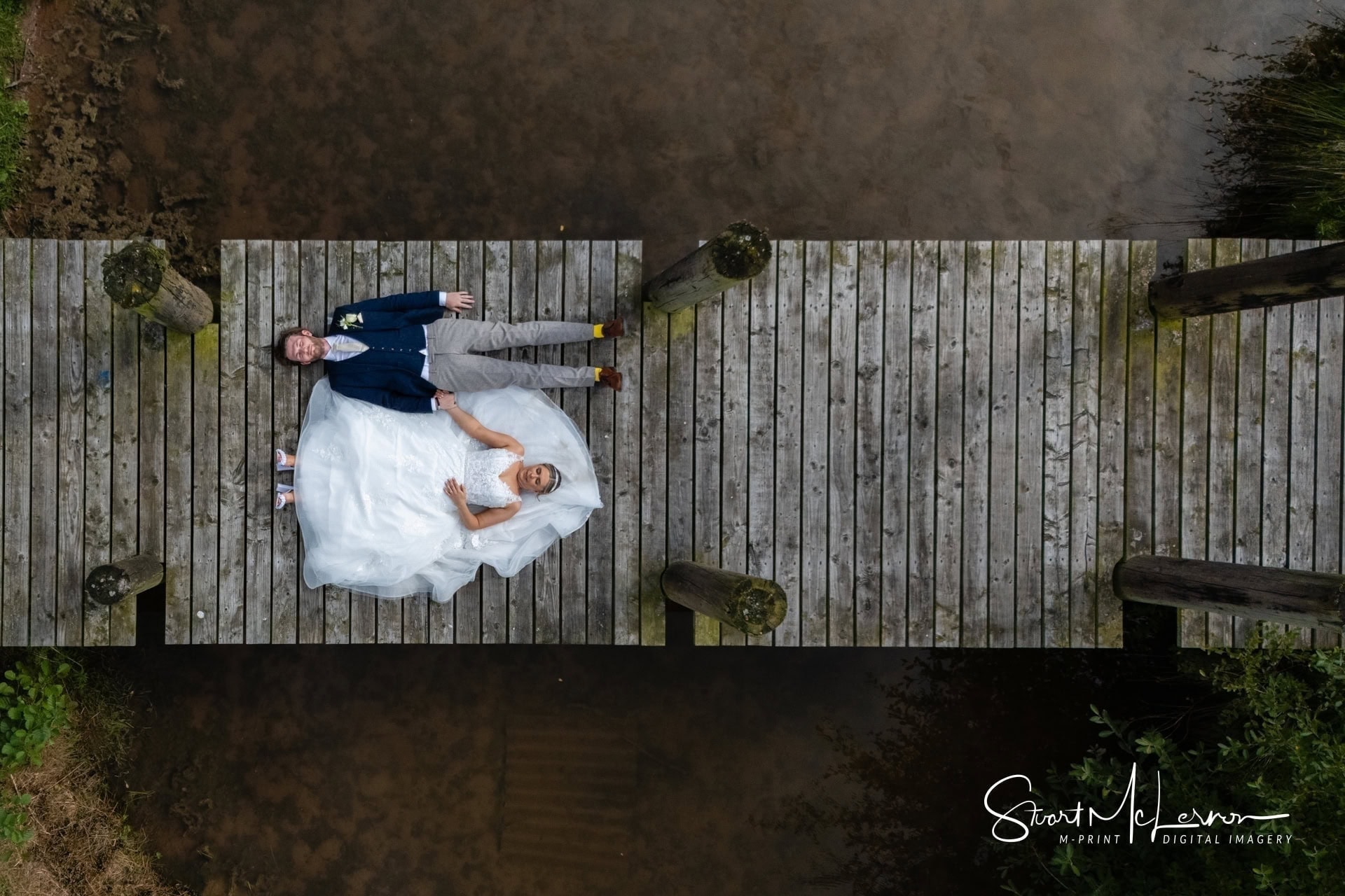 The bride and groom pose on the pier for a portrait on the lake at Alcumlow Wedding Barn.