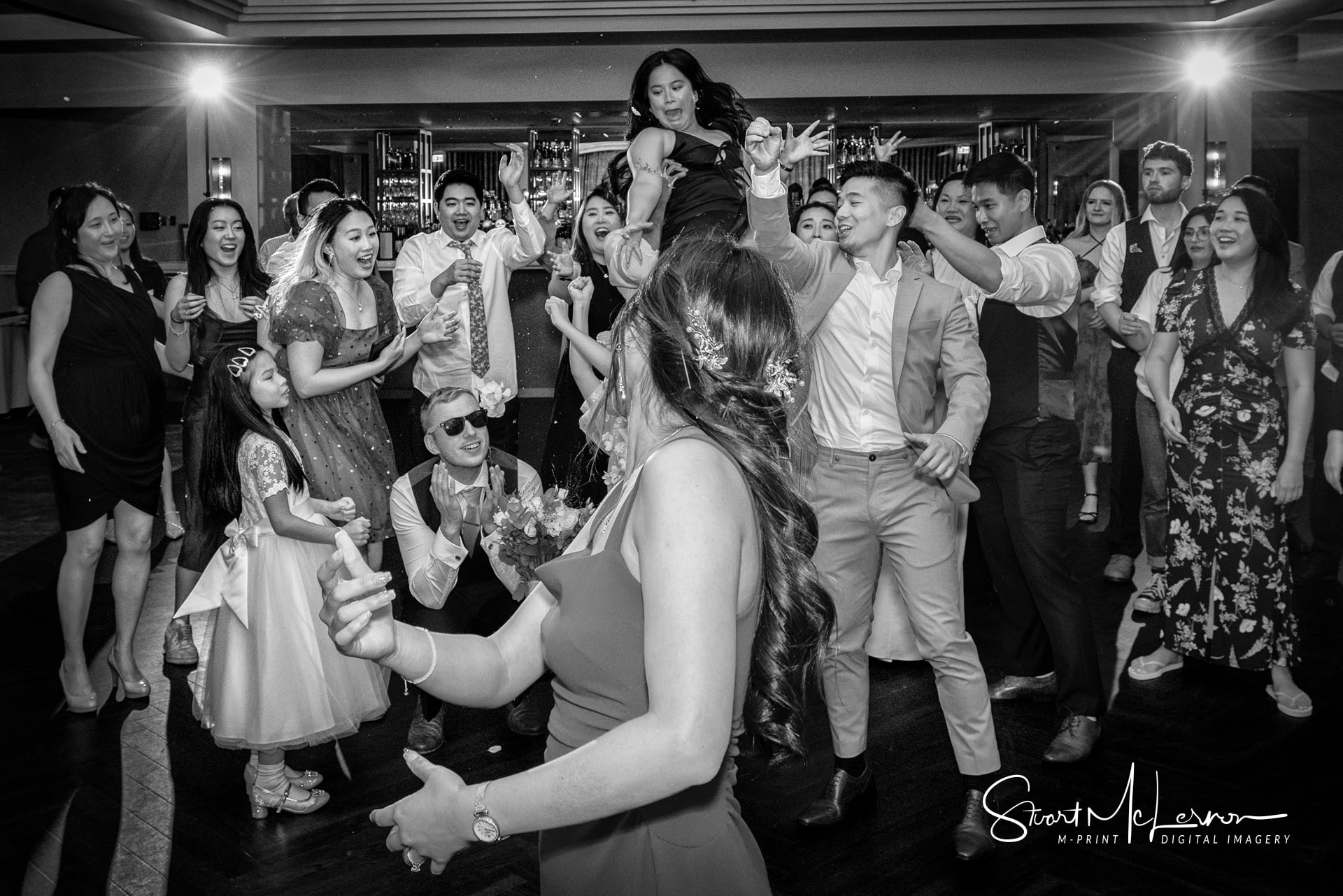 The wedding guests scramble to catch the wedding bouquet thrown by the bride