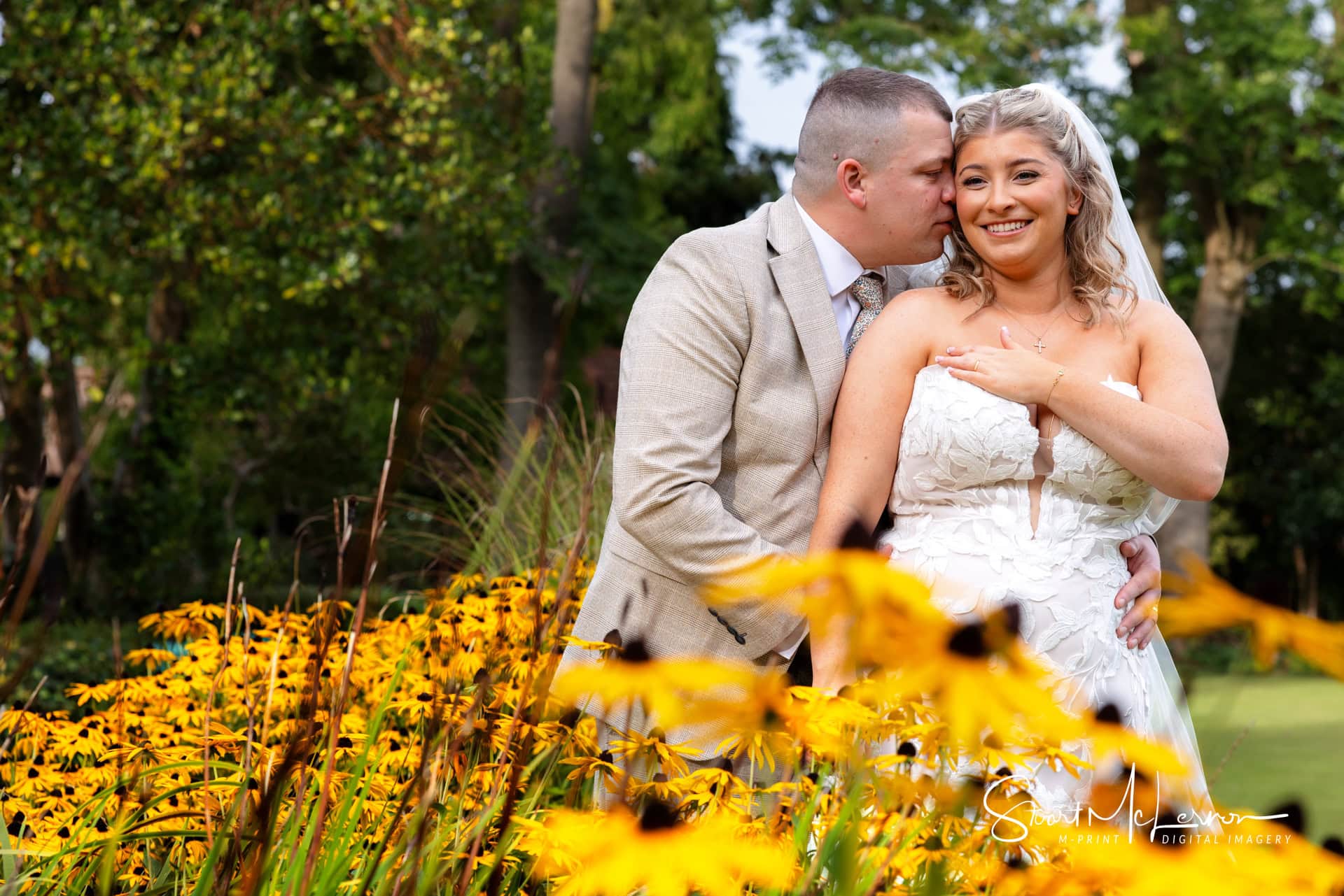 The groom nuzzles up to his bride amongst the flowers in Heaton Moor Park