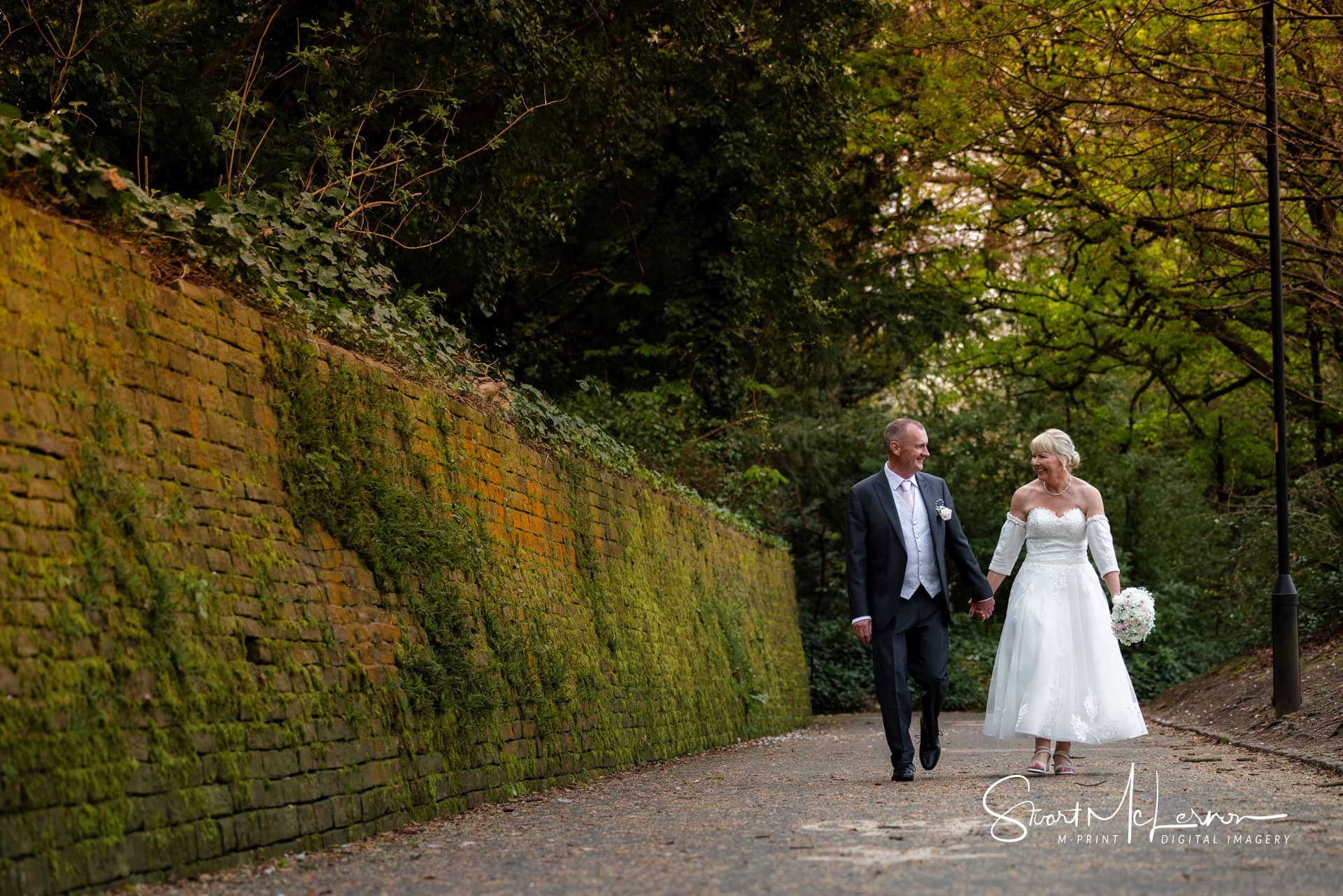 The wedding couple walk hand-in-hand outside the grounds of The Village Hotel Cheadle.